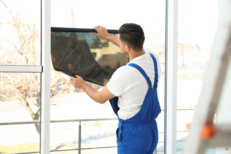 Professioneller Arbeiter, der Fenster mit Folie im Innenbereich tönt